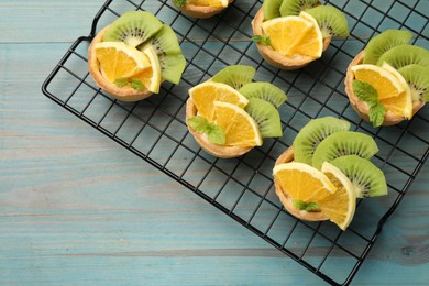 Photo of Tartlets with fruits and mint on light blue wooden table, top view. Delicious dessert