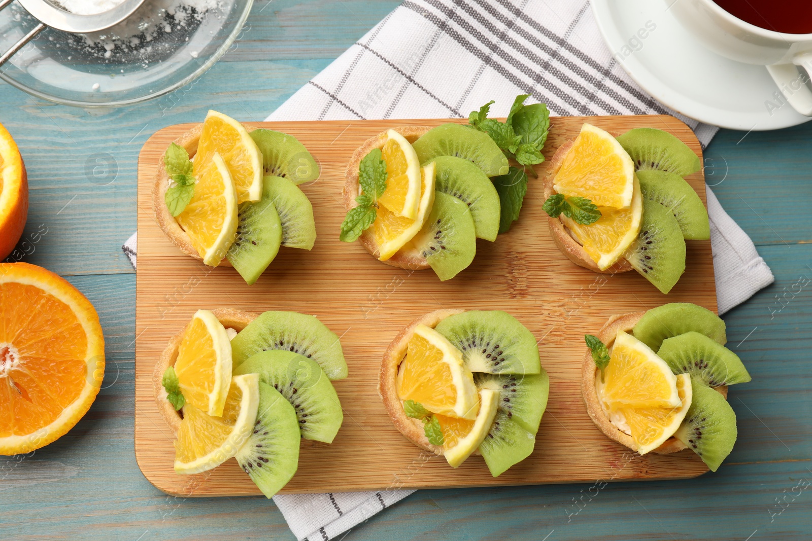 Tartlets with fruits, mint and tea on light blue wooden table, flat lay. Delicious dessert Photo of Tartlets with fruits, mint and tea on light blue wooden table, flat lay. Delicious dessert