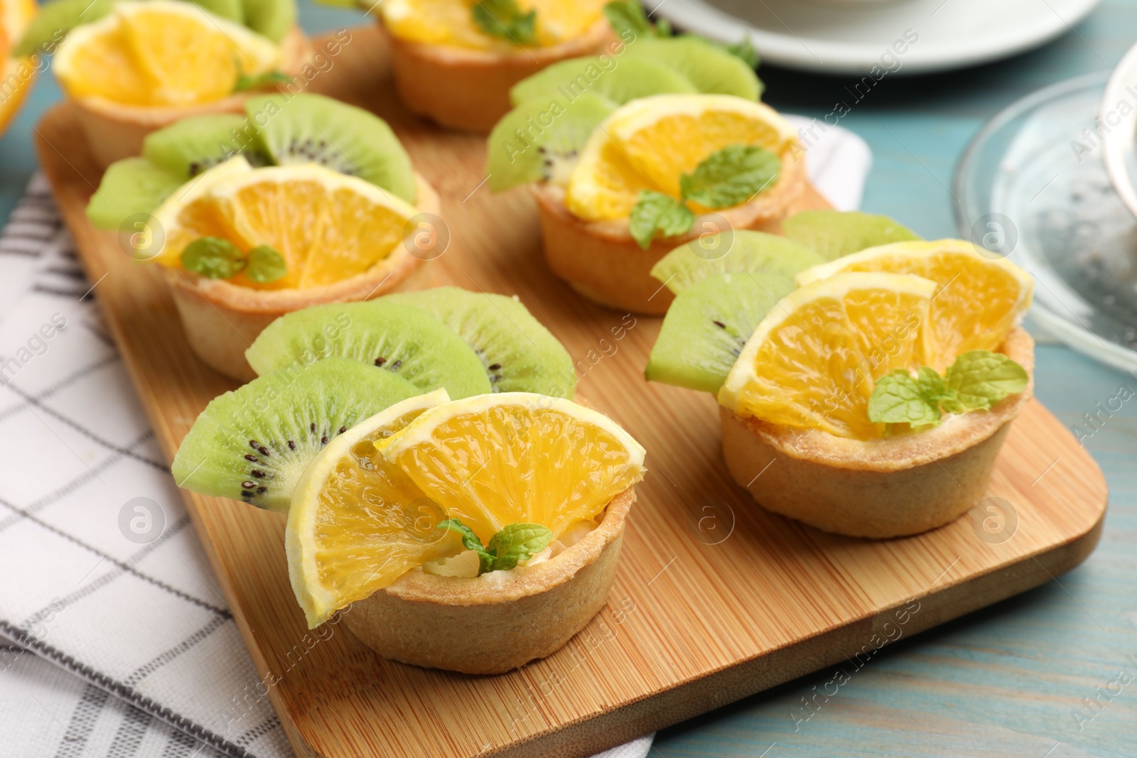 Photo of Tartlets with fruits and mint on light blue wooden table, closeup. Delicious dessert