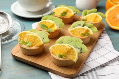 Photo of Tartlets with fruits and mint on light blue wooden table, closeup. Delicious dessert