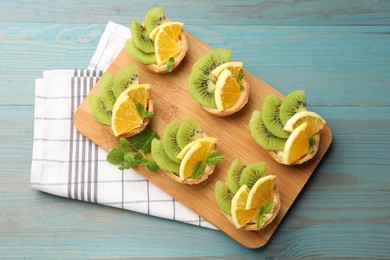 Photo of Tartlets with fruits and mint on light blue wooden table, top view. Delicious dessert