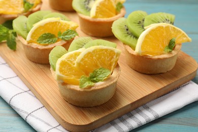 Photo of Tartlets with fruits and mint on light blue wooden table, closeup. Delicious dessert