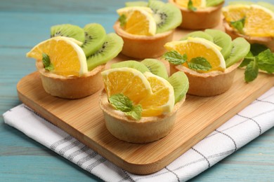 Photo of Tartlets with fruits and mint on light blue wooden table, closeup. Delicious dessert