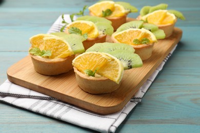 Photo of Tartlets with fruits and mint on light blue wooden table, closeup. Delicious dessert