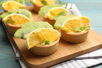 Photo of Tartlets with fruits and mint on light blue wooden table, closeup. Delicious dessert