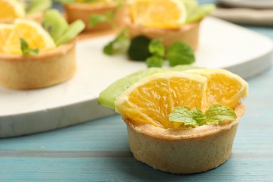 Photo of Tartlets with fruits and mint on light blue wooden table, closeup. Delicious dessert