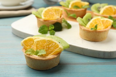 Photo of Tartlets with fruits and mint on light blue wooden table, closeup. Delicious dessert