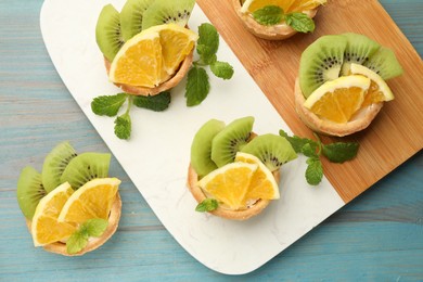 Photo of Tartlets with fruits and mint on light blue wooden table, top view. Delicious dessert