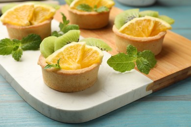 Photo of Tartlets with fruits and mint on light blue wooden table, closeup. Delicious dessert