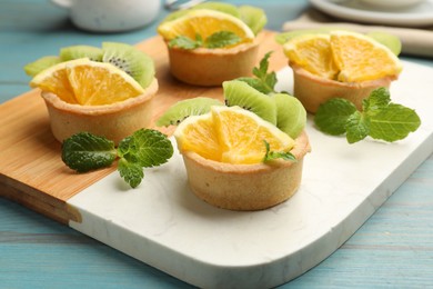 Photo of Tartlets with fruits and mint on light blue wooden table, closeup. Delicious dessert