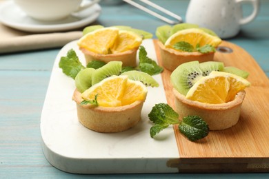 Photo of Tartlets with fruits and mint on light blue wooden table, closeup. Delicious dessert