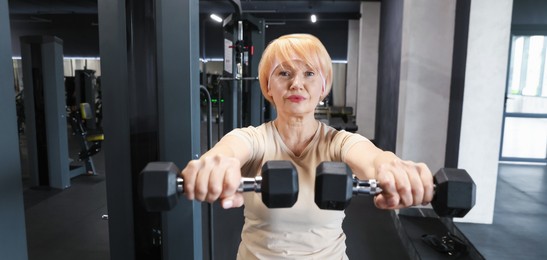 Photo of Senior woman training with dumbbells in gym