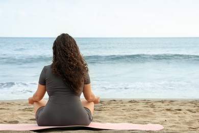 Photo of Woman meditating on sandy beach by sea, back view. Space for text