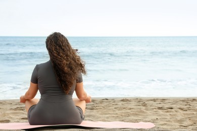 Photo of Woman meditating on sandy beach by sea, back view. Space for text