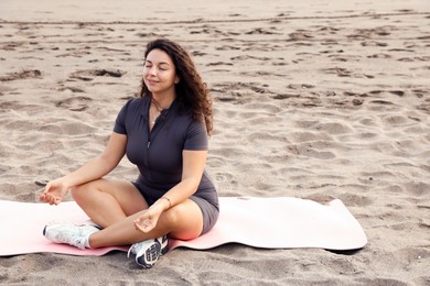 Photo of Beautiful young woman meditating on sandy beach, space for text