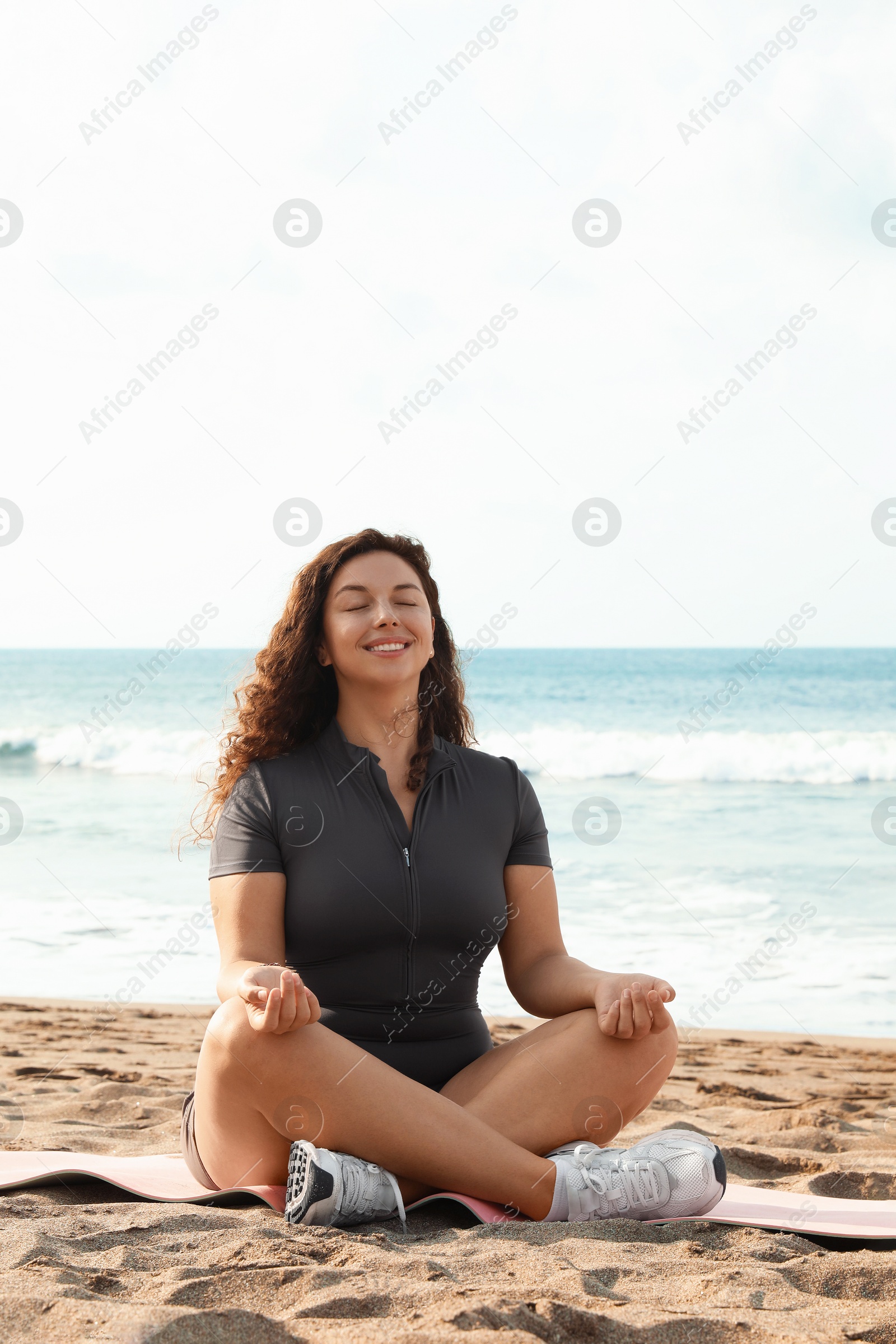 Woman meditating on sandy beach by sea Photo of Woman meditating on sandy beach by sea