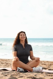 Photo of Woman meditating on sandy beach by sea