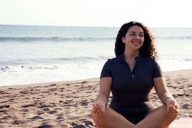 Photo of Woman meditating on sandy beach by sea, space for text