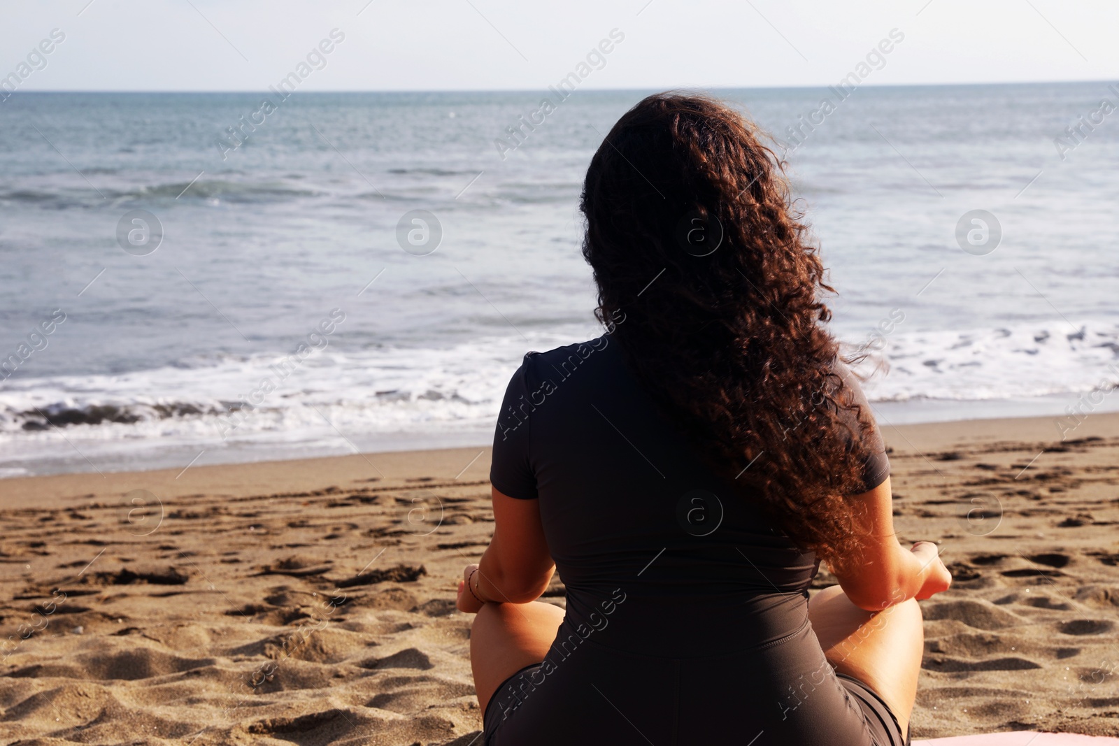 Woman meditating on sandy beach by sea, back view. Space for text Photo of Woman meditating on sandy beach by sea, back view. Space for text