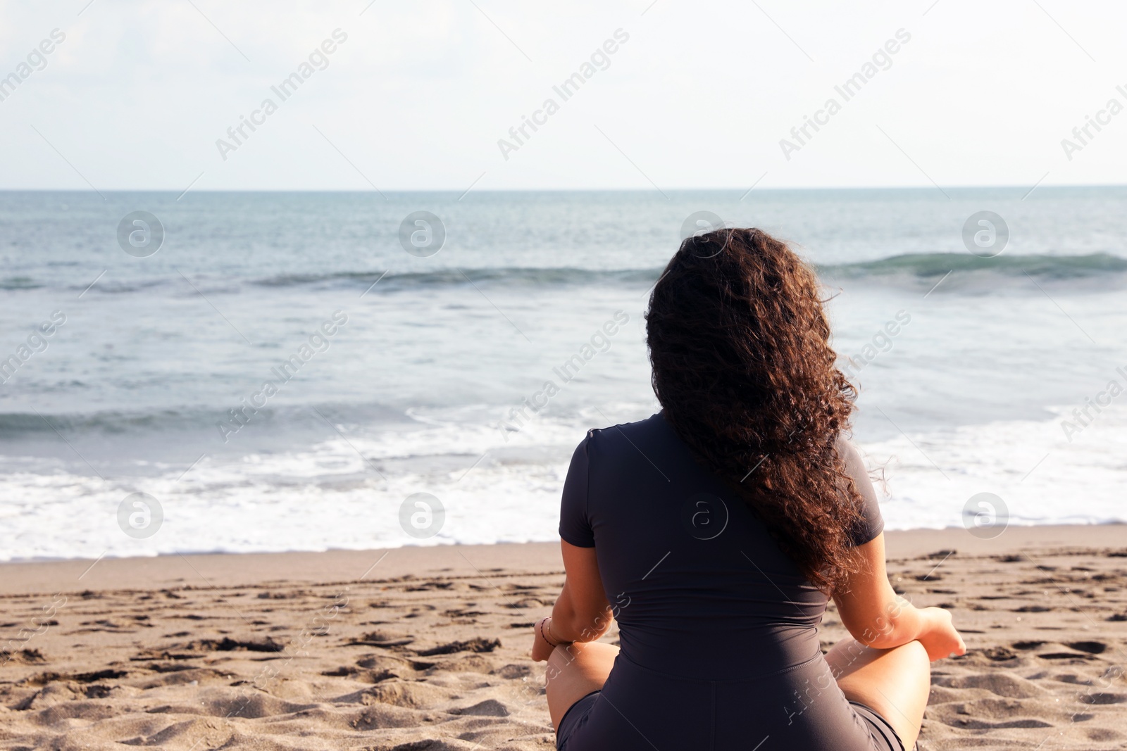 Woman meditating on sandy beach by sea, back view. Space for text Photo of Woman meditating on sandy beach by sea, back view. Space for text