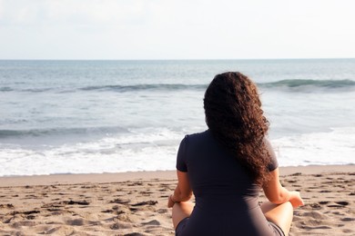 Photo of Woman meditating on sandy beach by sea, back view. Space for text