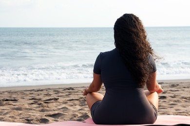 Photo of Woman meditating on sandy beach by sea, back view. Space for text