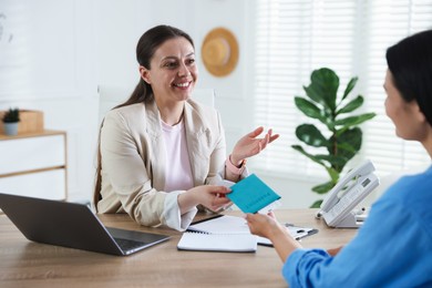 Photo of Travel agent giving passport with ticket to woman at wooden table in office