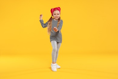 Photo of Cute little girl dancing on orange background