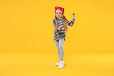 Photo of Cute little girl dancing on orange background