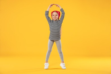 Photo of Cute little girl dancing on orange background