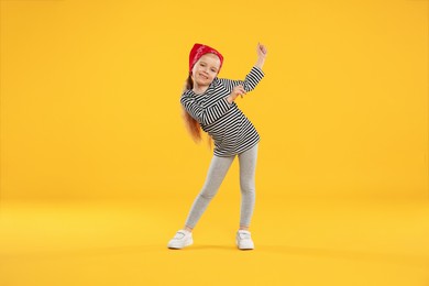 Photo of Cute little girl dancing on orange background