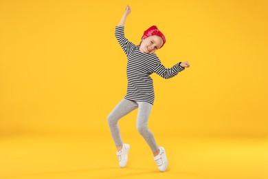 Photo of Cute little girl dancing on orange background