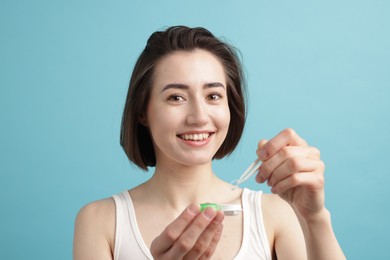 Photo of Woman taking contact lens out of case on light blue background