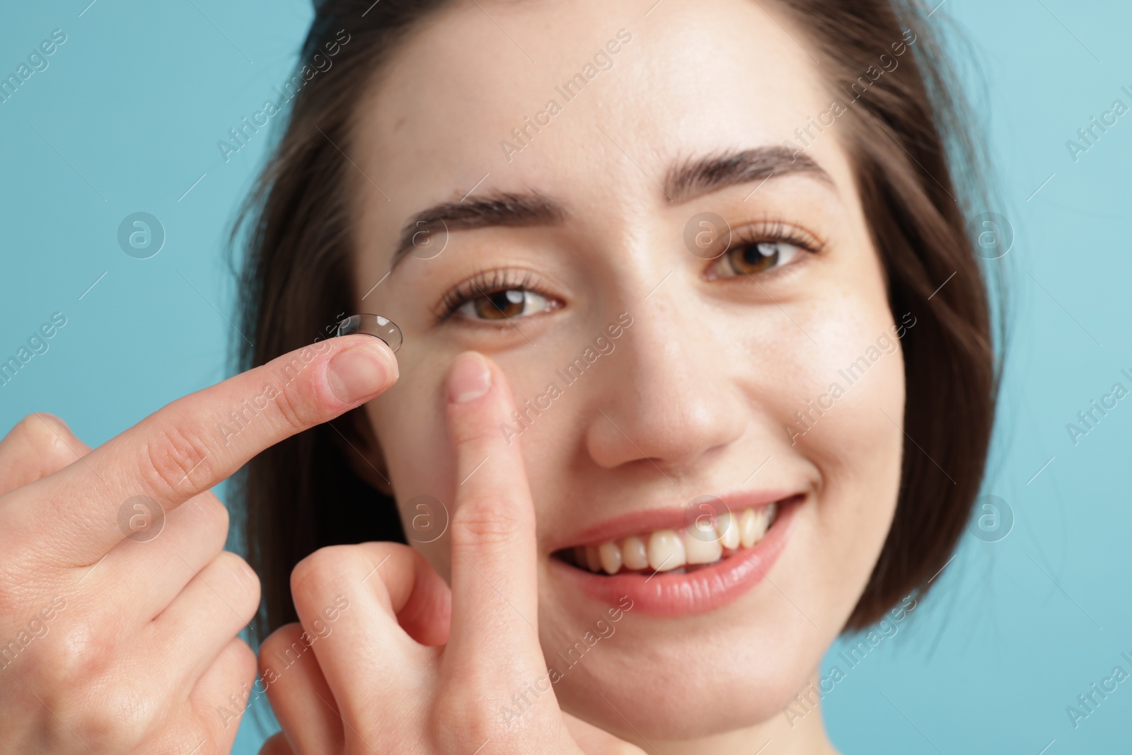 Woman putting in contact lens on light blue background, closeup Photo of Woman putting in contact lens on light blue background, closeup