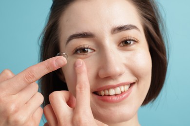 Photo of Woman putting in contact lens on light blue background, closeup
