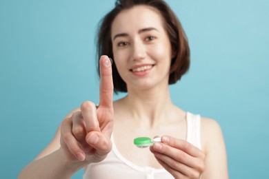 Photo of Woman with contact lens and case on light blue background, selective focus