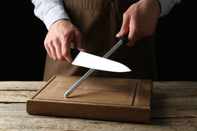 Photo of Man sharpening knife with sharpener on wooden table, closeup