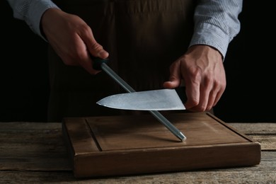 Photo of Man sharpening knife with sharpener on wooden table, closeup