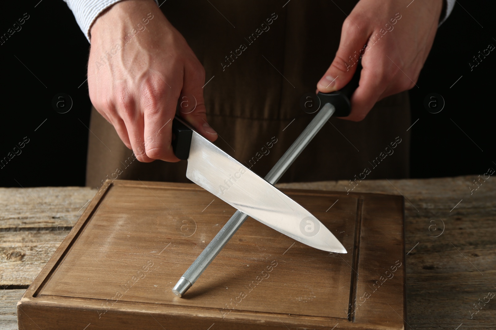 Man sharpening knife with sharpener on wooden table, closeup Photo of Man sharpening knife with sharpener on wooden table, closeup