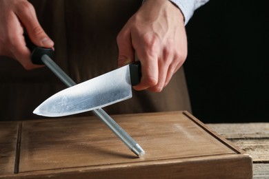 Photo of Man sharpening knife with sharpener on wooden table, closeup