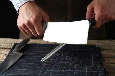 Photo of Man sharpening knife with sharpener on wooden table, closeup
