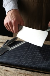 Photo of Man sharpening knife with sharpener on wooden table, closeup