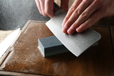 Photo of Man sharpening knife with sharpener on wooden table, closeup