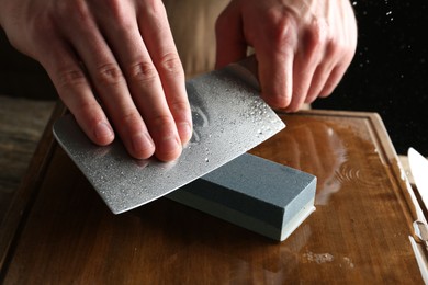 Photo of Man sharpening knife with sharpener on wooden table, closeup