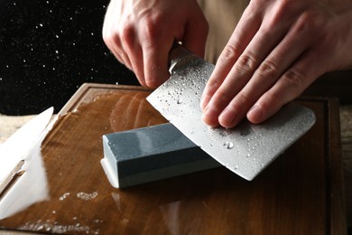Photo of Man sharpening knife with sharpener on wooden table, closeup