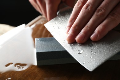Photo of Man sharpening knife with sharpener on wooden table, closeup