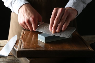 Photo of Man sharpening knife with sharpener on wooden table, closeup