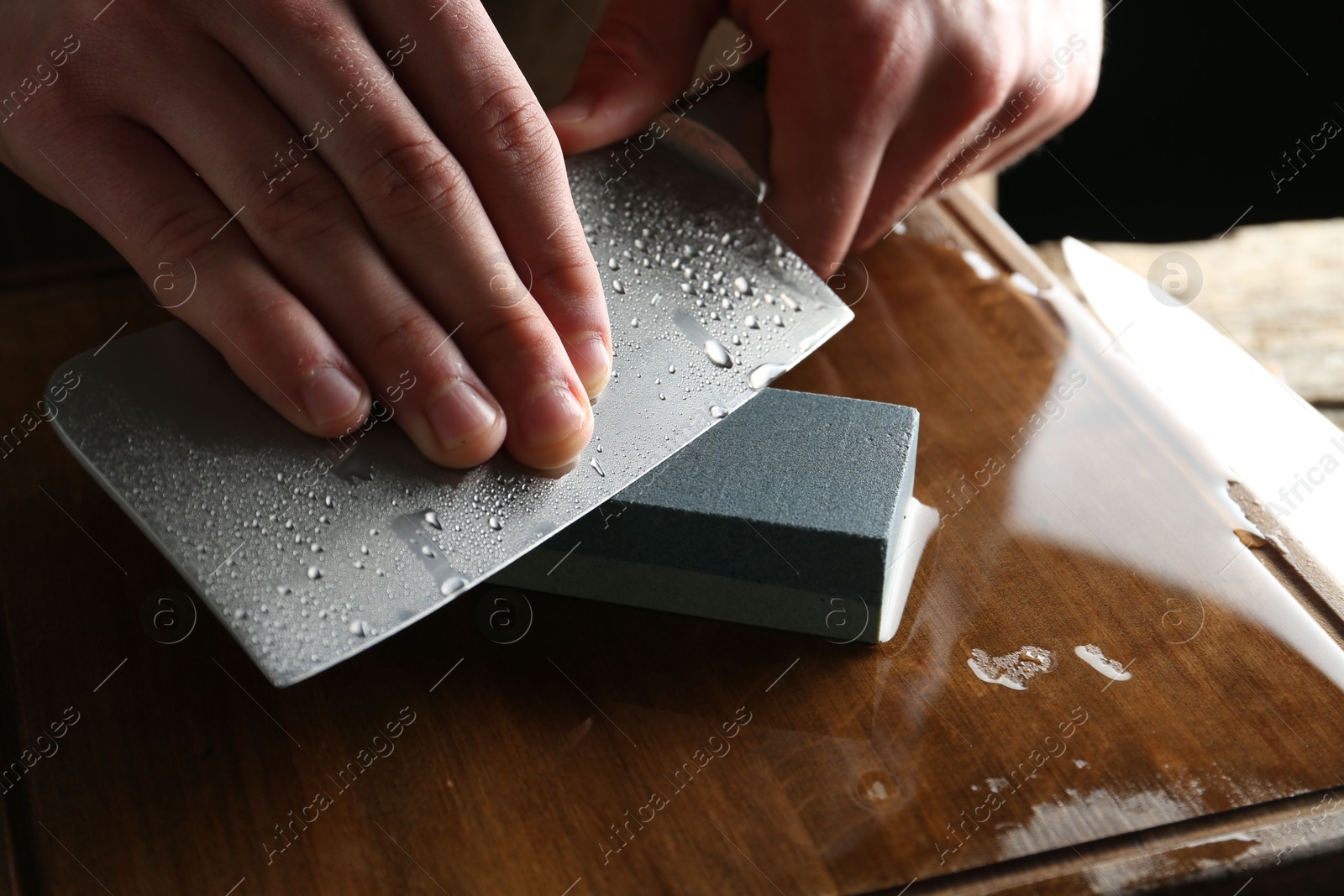 Man sharpening knife with sharpener on wooden table, closeup Photo of Man sharpening knife with sharpener on wooden table, closeup