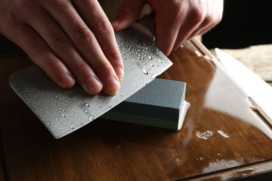 Photo of Man sharpening knife with sharpener on wooden table, closeup