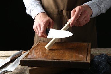 Photo of Man sharpening knife with sharpener on wooden table, closeup